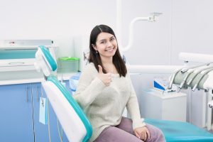Woman with healthy smile in dental chair giving thumbs up